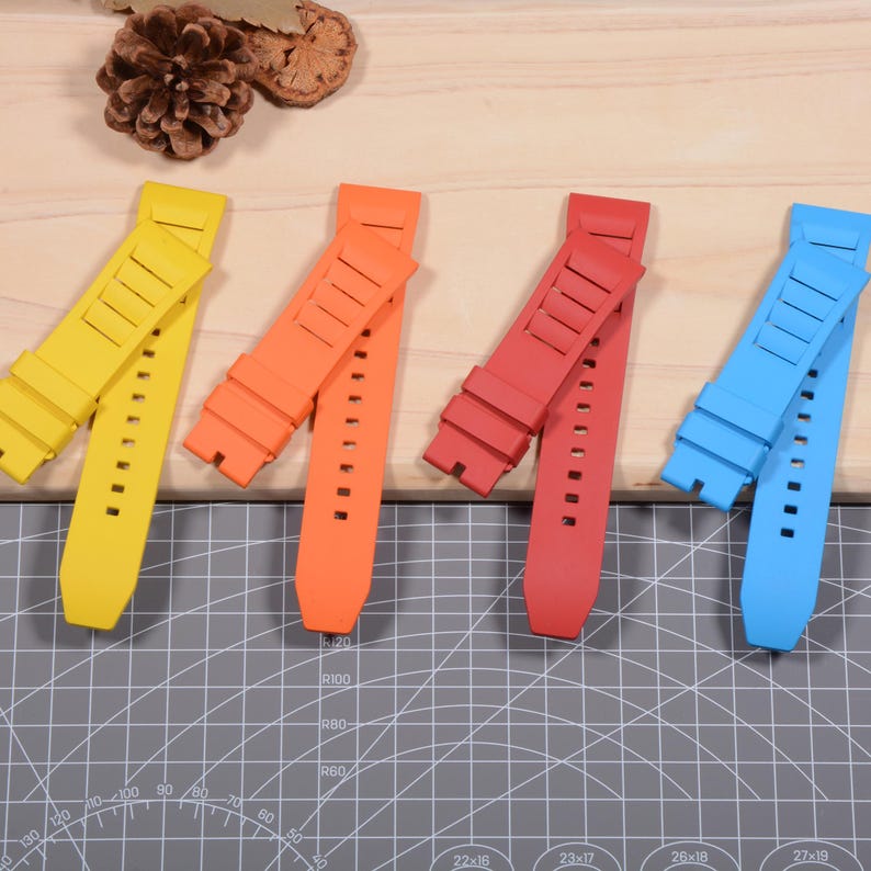 Op de afbeelding: Vier felgekleurde horlogebandjes in geel, oranje, rood en blauw worden getoond. Elke band heeft een reeks gaten voor aanpassing en een gestructureerd ontwerp. De bandjes zijn gemaakt van flexibel materiaal en liggen op een houten oppervlak.