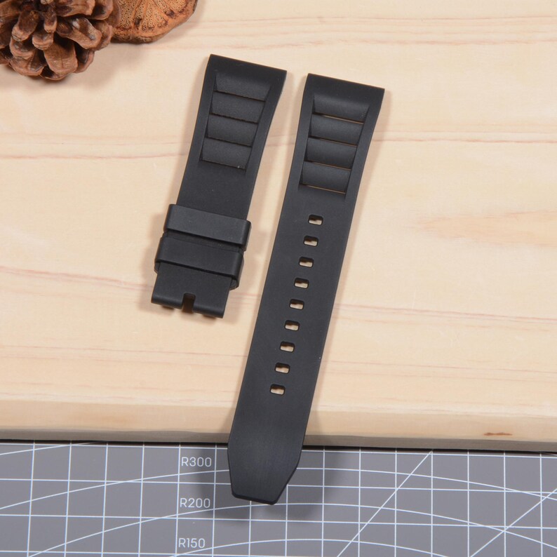 Op de afbeelding: Tweedelig zwart horlogebandje. De band heeft een gestructureerd ontwerp met horizontale ribbels en een reeks gaten voor aanpassing. De horlogeband is gemaakt van een flexibel materiaal en is ontworpen om aan een horlogekast te worden bevestigd.