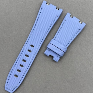 May include: A light blue watch strap set. The straps are made of a textured material with black stitching. The strap has multiple holes for adjustment and metal clasps.