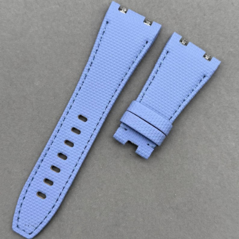 May include: A light blue watch strap set. The straps are made of a textured material with black stitching. The strap has multiple holes for adjustment and metal clasps.