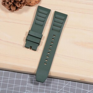 Op de afbeelding: Tweedelig donkergroene horlogeband. De band heeft een gestructureerd ontwerp met rechthoekige inkepingen en een reeks kleine gaatjes voor aanpassing. De horlogeband is gemaakt van een flexibel materiaal.