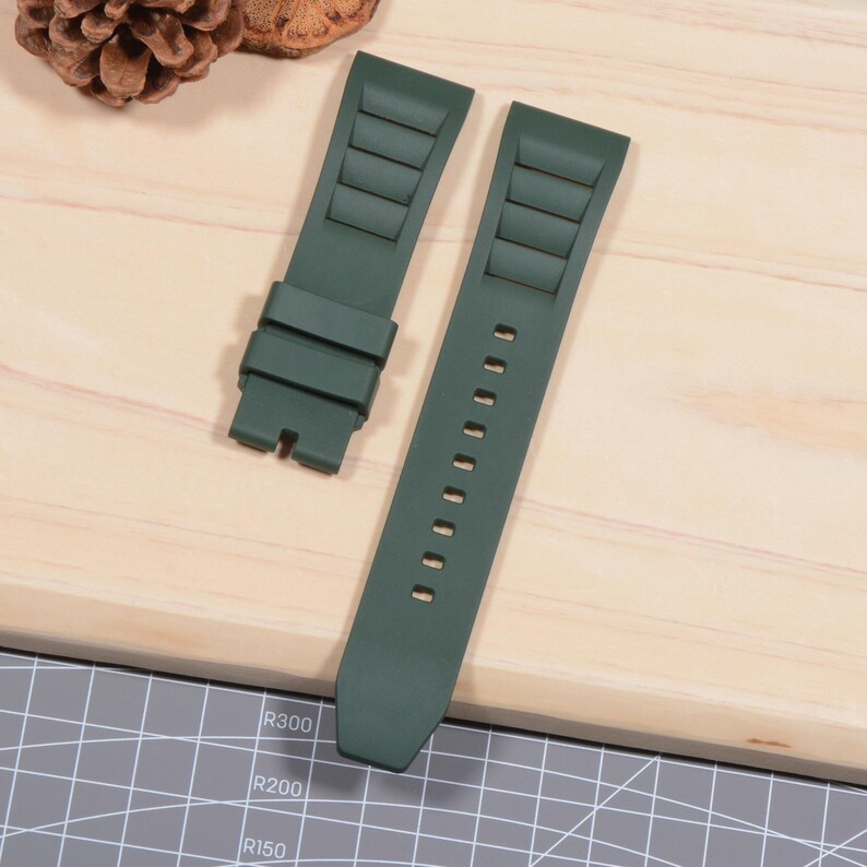 Op de afbeelding: Tweedelig donkergroene horlogeband. De band heeft een gestructureerd ontwerp met rechthoekige inkepingen en een reeks kleine gaatjes voor aanpassing. De horlogeband is gemaakt van een flexibel materiaal.