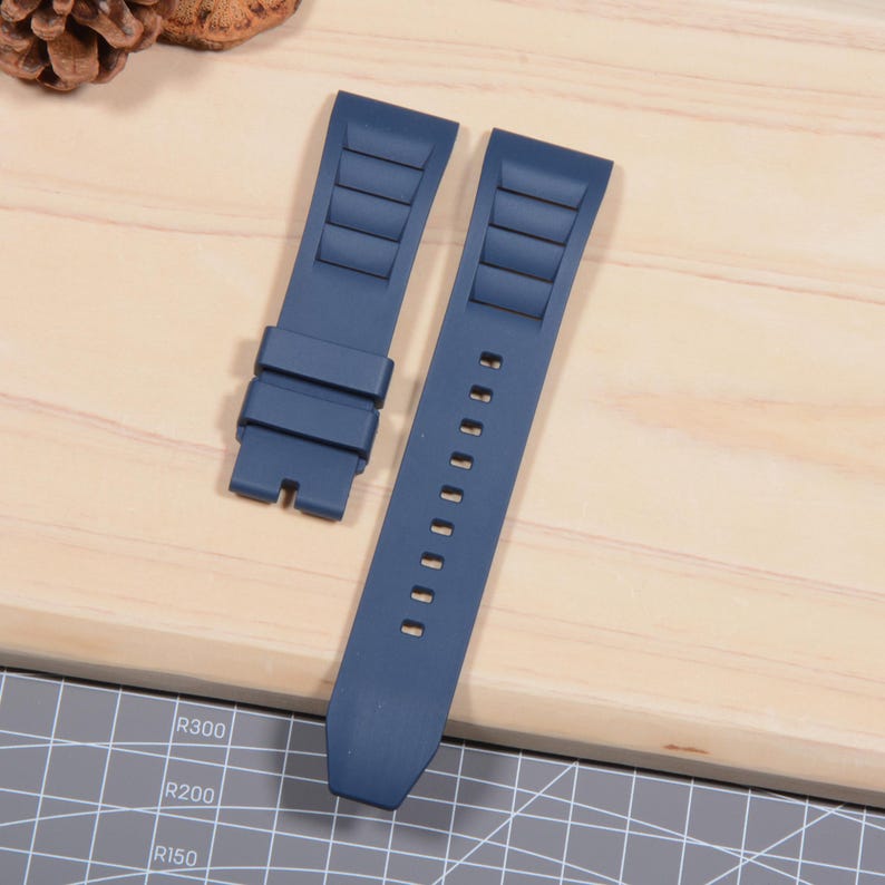 Op de afbeelding: Twee marineblauwe horlogebandjes. Elk bandje heeft een textuurontwerp met rechthoekige ribbels. E&eacute;n bandje heeft een gesp, de andere heeft verstelgaten. De bandjes zijn gemaakt van flexibel materiaal.