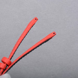 Puede incluir: Primer plano de dos correas de reloj rojas con la parte inferior negra. Las correas est&aacute;n anguladas entre s&iacute;, con peque&ntilde;os agujeros en las puntas. Las correas tienen una superficie texturizada y parecen estar hechas de un material flexible.