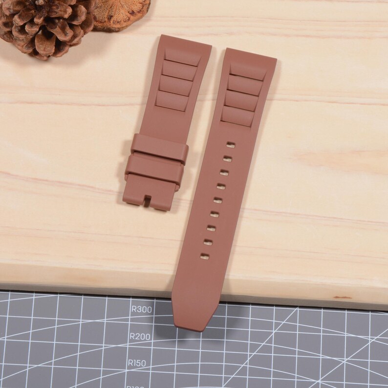 Op de afbeelding: Twee bruine horlogebandjes met een textuurontwerp. E&eacute;n bandje heeft een gesp en de andere heeft een reeks gaten voor aanpassing. De bandjes zijn gemaakt van flexibel materiaal en zijn ontworpen om aan een horlogekast te worden bevestigd.