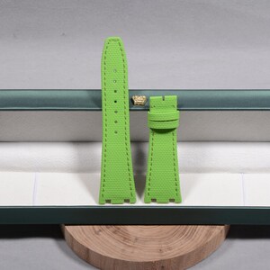 Puede incluir: Juego de correas de reloj verde brillante. Las correas est&aacute;n hechas de un material texturizado y presentan costuras en contraste. El juego incluye dos piezas, una con varios agujeros para ajuste y otra con una hebilla. Las correas se muestran dentro de una caja verde.