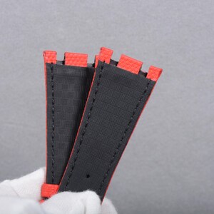 Puede incluir: Dos correas de reloj con una superficie negra texturizada y bordes rojos. Las correas est&aacute;n cosidas con hilo negro y tienen un dise&ntilde;o rectangular. Las correas est&aacute;n hechas de un material duradero.