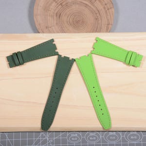 Puede incluir: Cuatro correas de reloj verdes, dispuestas sobre una superficie de madera. Dos correas son de color verde oscuro y dos son de color verde lima vibrante. Todas las correas tienen costuras y agujeros de ajuste. Las correas est&aacute;n dise&ntilde;adas para un reloj.
