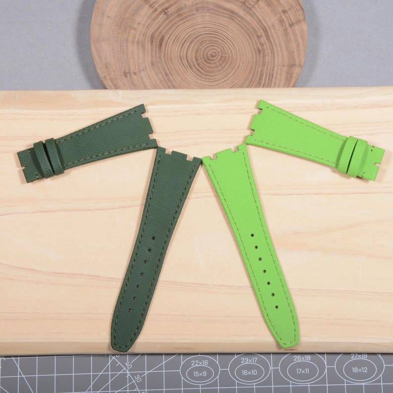 Puede incluir: Cuatro correas de reloj verdes, dispuestas sobre una superficie de madera. Dos correas son de color verde oscuro y dos son de color verde lima vibrante. Todas las correas tienen costuras y agujeros de ajuste. Las correas est&aacute;n dise&ntilde;adas para un reloj.
