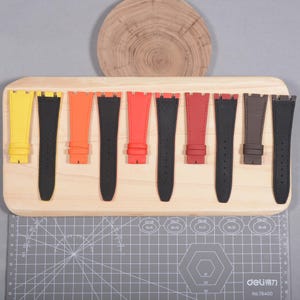 Puede incluir: Una colecci&oacute;n de correas de reloj coloridas exhibidas en una tabla de madera. Las correas vienen en varios colores, incluyendo amarillo, naranja, rojo y marr&oacute;n, con correas negras intercaladas. Las correas son de cuero y tienen una apariencia texturizada.