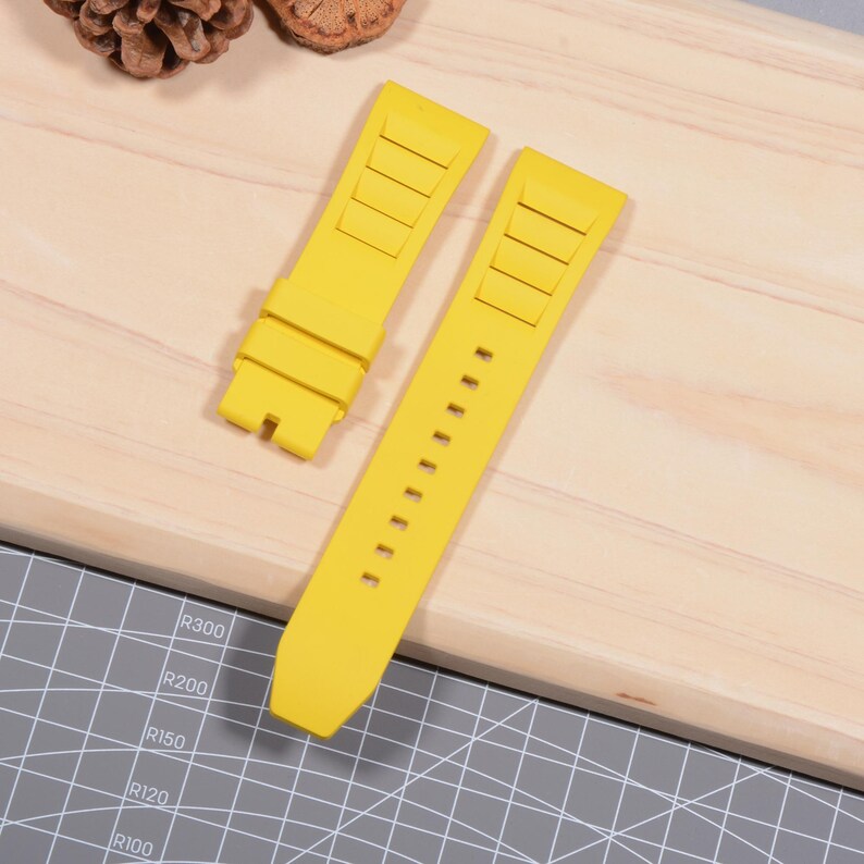 Op de afbeelding: Twee felgele horlogebandjes worden getoond op een houten oppervlak. E&eacute;n bandje is losgemaakt en toont de pengaten, terwijl de andere is aangesloten. De bandjes hebben een gestructureerd ontwerp en zijn gemaakt van flexibel materiaal.