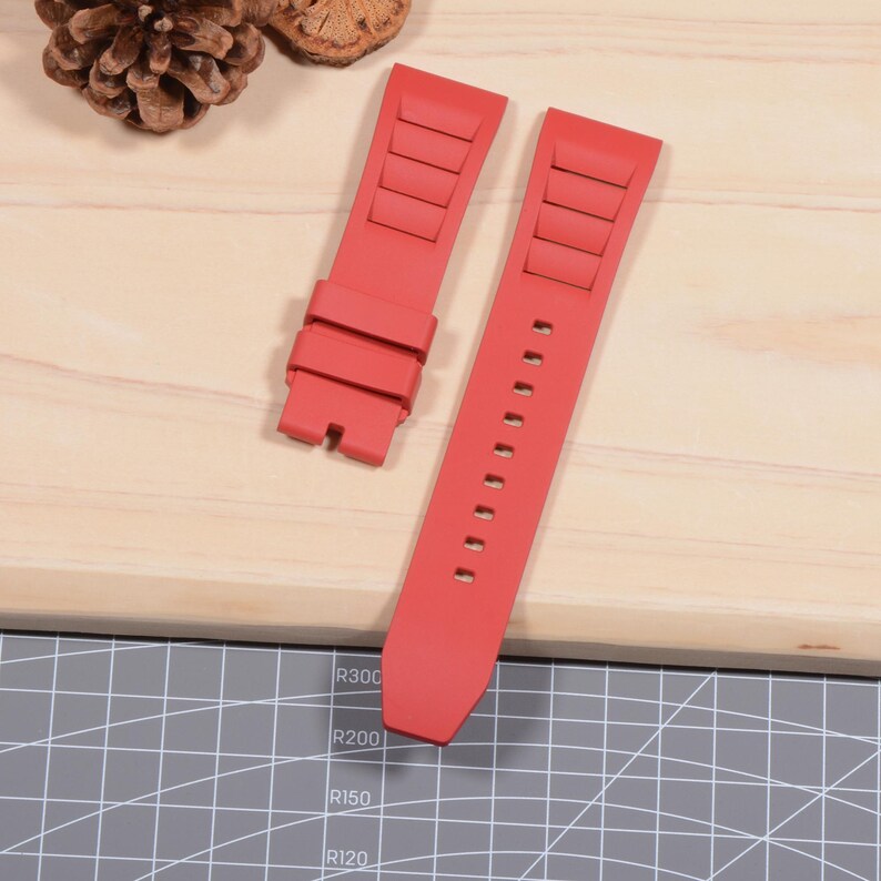 Op de afbeelding: Twee felrode horlogebandjes. E&eacute;n bandje heeft een reeks rechthoekige ribbels, terwijl de andere een reeks kleine gaatjes heeft. De bandjes zijn gemaakt van flexibel materiaal en zijn ontworpen om aan een horloge te bevestigen.