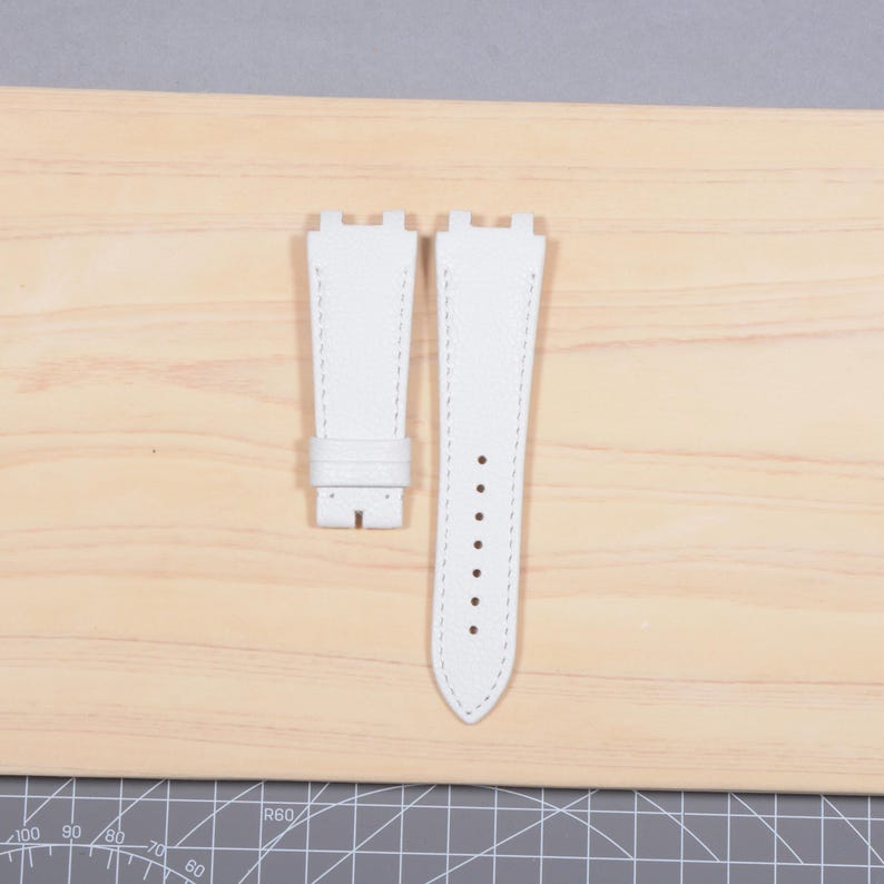 May include: A pair of white leather watch straps with white stitching. The straps are shown on a light wood surface. One strap has a buckle, and the other has several holes for adjustment. The straps are new and unused.