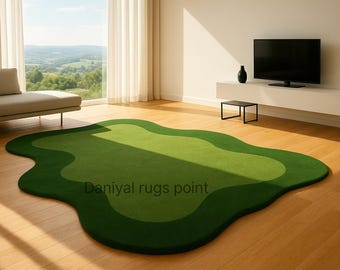 Può includere: Un tappeto dalla forma organica irregolare caratterizzato da un design a strati in due tonalità di verde, con un bordo verde scuro e un centro verde più chiaro. Il testo 'Daniyal rugs point' è stampato in nero sulla superficie del tappeto.