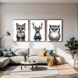 Könnte beinhalten: Drei gerahmte Wandbilder mit einem grauen Fuchs, der eine Teetasse hält, einem Hirsch mit einem blauen Buch und einer Eule mit schwarzer Brille. Die Illustrationen sind in Graustufen gehalten, mit dezenten Farbakzenten an Tasse und Buch.