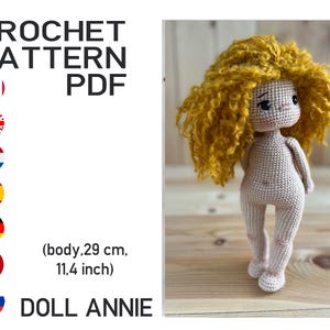 Peut inclure: Une poupée crochetée nommée Annie avec des cheveux bouclés jaunes. Le corps de la poupée est beige et mesure 29 cm. L'image comprend le texte "CROCHET PATTERN PDF" et une liste de drapeaux. La poupée est debout.