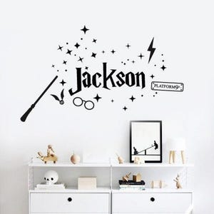 May include: Black wall sticker with the name "Jackson" in a decorative font, alongside a wand, glasses, stars, and a lightning bolt. Includes a "Platform 9 3/4" sign. Ideal for themed room decor.