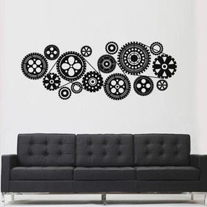May include: Black wall decal featuring a collection of interconnected gears in various sizes and designs. The gears are arranged in a horizontal, flowing pattern. Below the decal is a black, tufted sofa.