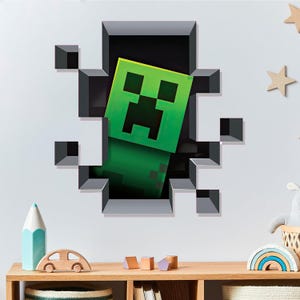以下が含まれることがあります： 壁から現れる緑と黒のMinecraftクリーパーのキャラクター。壁は、グレーと黒のピクセル化されたブロックで3D効果があります。クリーパーは正方形の頭と体を持っています。これはウォールステッカーです。