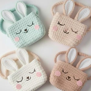 May include: Four crochet bunny bags in pastel colors: light blue, beige, white, and brown. Each bag features a bunny face with closed eyes, pink cheeks, and long ears. The bags have a braided handle and are perfect for Easter.