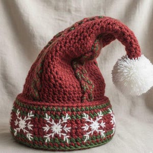May include: A handmade, red crocheted hat with a white pom-pom and green accents. The hat features a snowflake pattern around the base and a cable knit design. This festive hat is perfect for the holiday season.