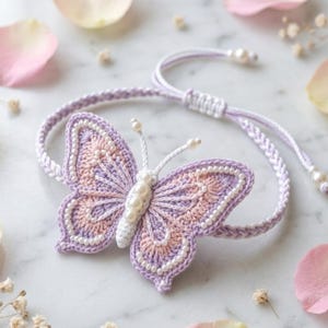 May include: A bracelet featuring a crocheted butterfly centrepiece in shades of lavender and soft peach. The butterfly is accented with small white beads along its wings and body, with two antennae tipped with beads. The band is a braided lavender cord.