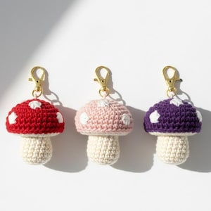 Può includere: Tre portachiavi a forma di fungo all'uncinetto, rossi, rosa e viola, ciascuno con macchie bianche e uno stelo color crema. I portachiavi hanno chiusure color oro.