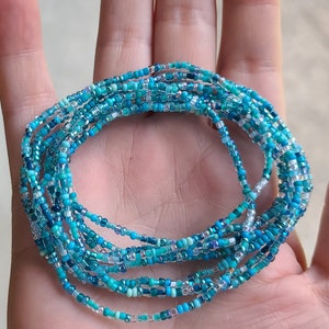 May include: A multi-strand beaded bracelet with blue and turquoise beads. The bracelet is made of small, round beads and is wrapped around a hand.