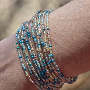 May include: A multi-strand beaded bracelet with turquoise, light blue, and pink beads. The bracelet is wrapped around a person's wrist.