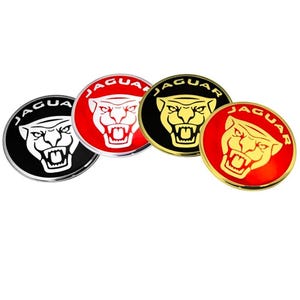 May include: Four Jaguar emblem badges in a circular shape. The badges feature a jaguar head with the word "JAGUAR" around the edge. The badges are in black, red, and gold colors with a chrome finish.