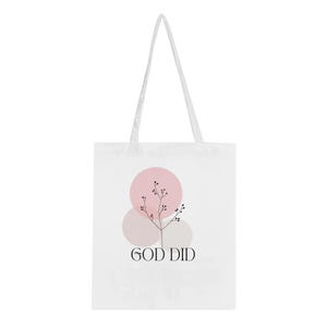 May include: White tote bag with a minimalist design. The bag features a pink circle, a light gray circle, and a sprig of black leaves. The words "GOD DID" are printed in black at the bottom of the bag.