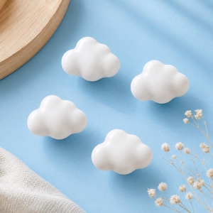 Puede incluir: Cuatro pomos blancos con forma de nube sobre una superficie azul claro. Los pomos son brillantes y tridimensionales. Un elemento de madera y una ramita de flores blancas están en el fondo. Adecuado para muebles.