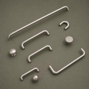 May include: A selection of brushed nickel cabinet hardware, including bar pulls, curved pulls, and round knobs. The hardware is displayed on a muted green background, showcasing the different designs and sizes. Measurements are in cm.