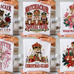 May include: A collection of six white t-shirts featuring colorful graphic prints of nutcrackers. Designs include text such as Nutcracker Midnight Club, Nutcracker Social Club, Sugar Plum Society, Coquette, The Christmas Guard, and a nutcracker with gifts.