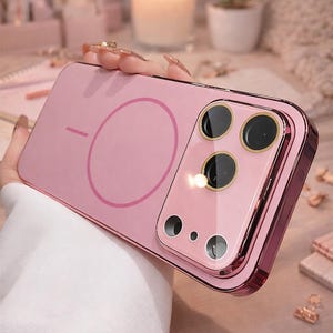 May include: A pink phone case with a matching camera lens protector. The case has a circular design on the back and a metallic pink frame. The camera protector has three large and two small lens openings.