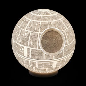 Könnte beinhalten: Eine kugelförmige Lampe mit einer detaillierten, beleuchteten Oberflächenstruktur, die an eine Raumstation erinnert. Das Design umfasst eine markante kreisförmige, konkave Vertiefung in der oberen Hälfte und gitterartige Muster.