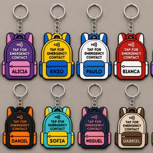 Pode incluir: Uma coleção de doze porta-chaves em forma de mochila, cada um com um anel e corrente de metal. Os porta-chaves exibem o texto TAP FOR EMERGENCY CONTACT e um nome único no bolso frontal, incluindo Júlia, Alicia, Enzo, Paulo, Bianca, Lais, Pietro, Daniel, Sofia, Miguel, Gabriel e Helena.