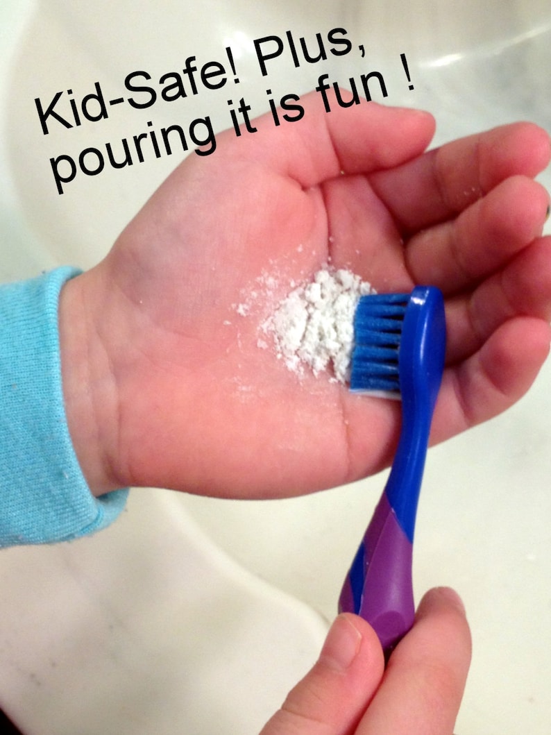 May include: A child's hand holding a blue and purple toothbrush with white powder and the text "Kid-Safe! Plus, pouring it is fun!" The toothbrush has blue bristles and a purple handle.