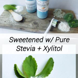May include: Two blue bottles of tooth powder and a toothbrush are displayed on a wooden surface. The bottles have white labels. The text "Sweetened w/ Pure Stevia + Xylitol" is also visible. A wooden spoon holds a white powder.