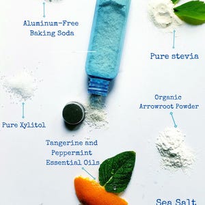 May include: Image showing ingredients for natural tooth powder: aluminum-free baking soda, pure stevia, pure xylitol, tangerine and peppermint essential oils, organic arrowroot powder, sea salt, and bentonite clay. A blue container is in the centre.