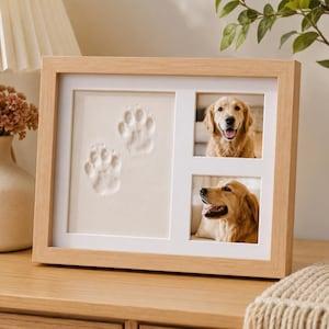 May include: A light wood rectangular picture frame featuring a white mount with three apertures. The left section displays two embossed paw prints on a cream background, while the two right sections contain photographs of a golden retriever dog.