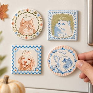 Pode incluir: Quatro ímanes decorativos com retratos ilustrados de animais de estimação. Dois são circulares e dois quadrados, cada um exibindo um gato ou cão com o nome escrito acima: Lemon, Luna, Cookie e Murphy. Os designs incluem bordas florais e xadrez.