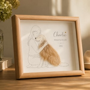 Può includere: Una cornice in legno chiaro contenente un disegno al tratto di una persona che abbraccia un cane. Il cane ha un'applicazione di pelliccia testurizzata color marrone dorato. Il testo recita Charlie, Always by my side e 2026, con un cuoricino.