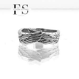 Puede incluir: Un anillo plateado con un dise&ntilde;o detallado de alas. El anillo es muy reflectante, con el dise&ntilde;o de alas envolviendo la banda. La imagen incluye el texto "FLACON SITTANO JEWELRY" en la esquina superior izquierda.