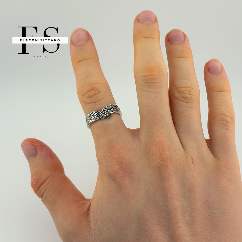 Puede incluir: Un anillo de plata con un dise&ntilde;o detallado de plumas. El anillo se lleva en un dedo, mostrando el intrincado patr&oacute;n del trabajo en metal. El anillo es una joya.