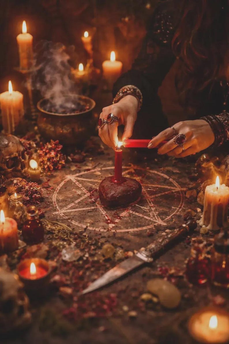 K&ouml;nnte beinhalten: Eine mystische Szene mit Kerzen, einem Pentagramm und einem herzf&ouml;rmigen Objekt. Eine Person z&uuml;ndet eine rote Kerze an, umgeben von anderen brennenden Kerzen, einem Kessel und einem Messer. Die Szene spielt auf einem Tisch mit getrockneten Kr&auml;utern und Blumen.