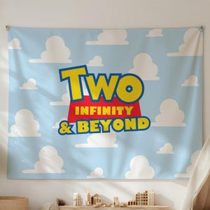 Op de afbeelding: Een lichtblauw wandtapijt met witte wolken en de tekst "TWO INFINITY & BEYOND" in geel, rood en blauw. Het wandtapijt hangt aan een witte muur. Een kleine tipi en een houten bank staan op de voorgrond.