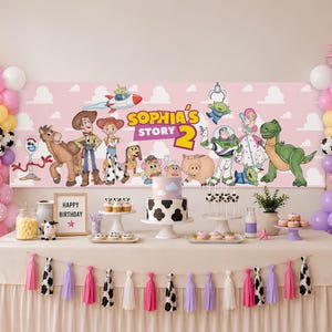 May include: A party backdrop banner featuring Toy Story characters and the text Sophia's Story 2, flanked by pink, yellow, purple, and white balloon arches. The table is decorated with a cow-print cake, cupcakes, and a tassel garland.