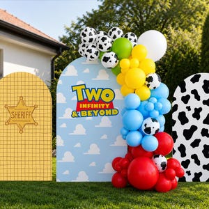 May include: Three arched backdrop panels featuring a yellow sheriff badge design, a light blue sky with white clouds and the text Two Infinity & Beyond, and a black and white cow print pattern, decorated with a multi-colored balloon garland.