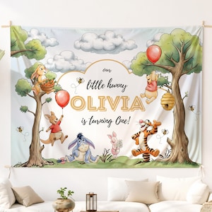 May include: A birthday banner with illustrations of Winnie the Pooh characters. The banner reads "our little hunny OLIVIA is turning One!" with images of Pooh, Tigger, Eeyore, and other characters, along with balloons and bees.